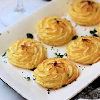 Close up of cooked Duchess Potatoes on a white serving dish.