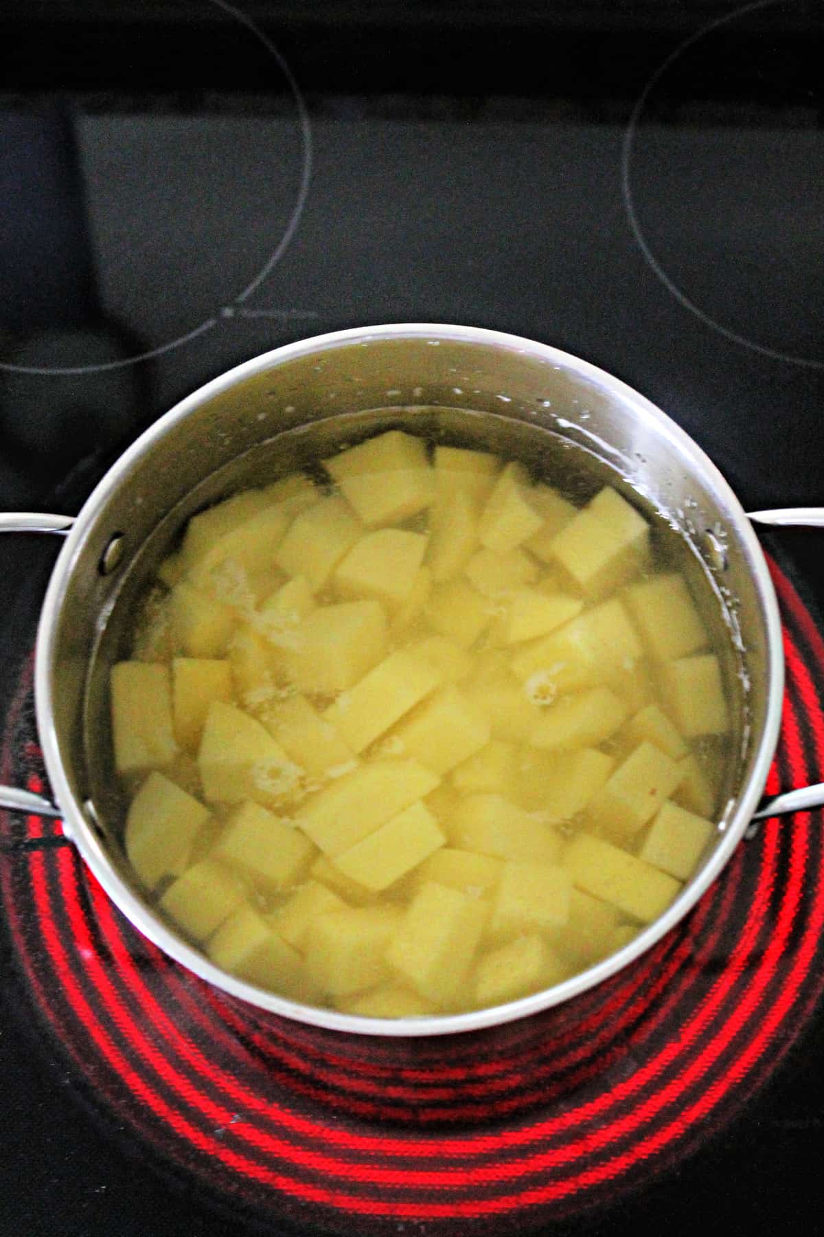 Overhead shot of diced potatoes in a pot with water on stovetop.