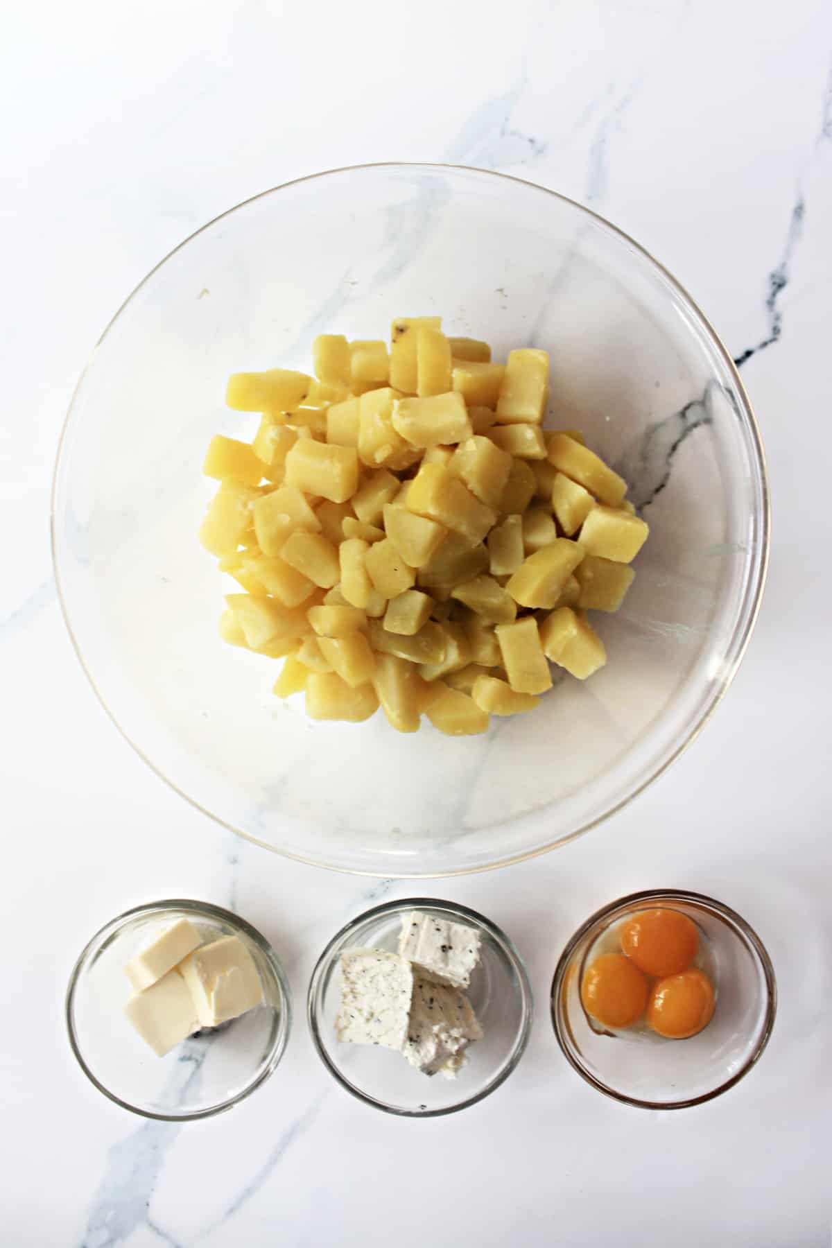 Overhead shot of ingredients for Duchess Potatoes -- cooked diced potatoes, egg yolks, Boursin cheese, and butter.