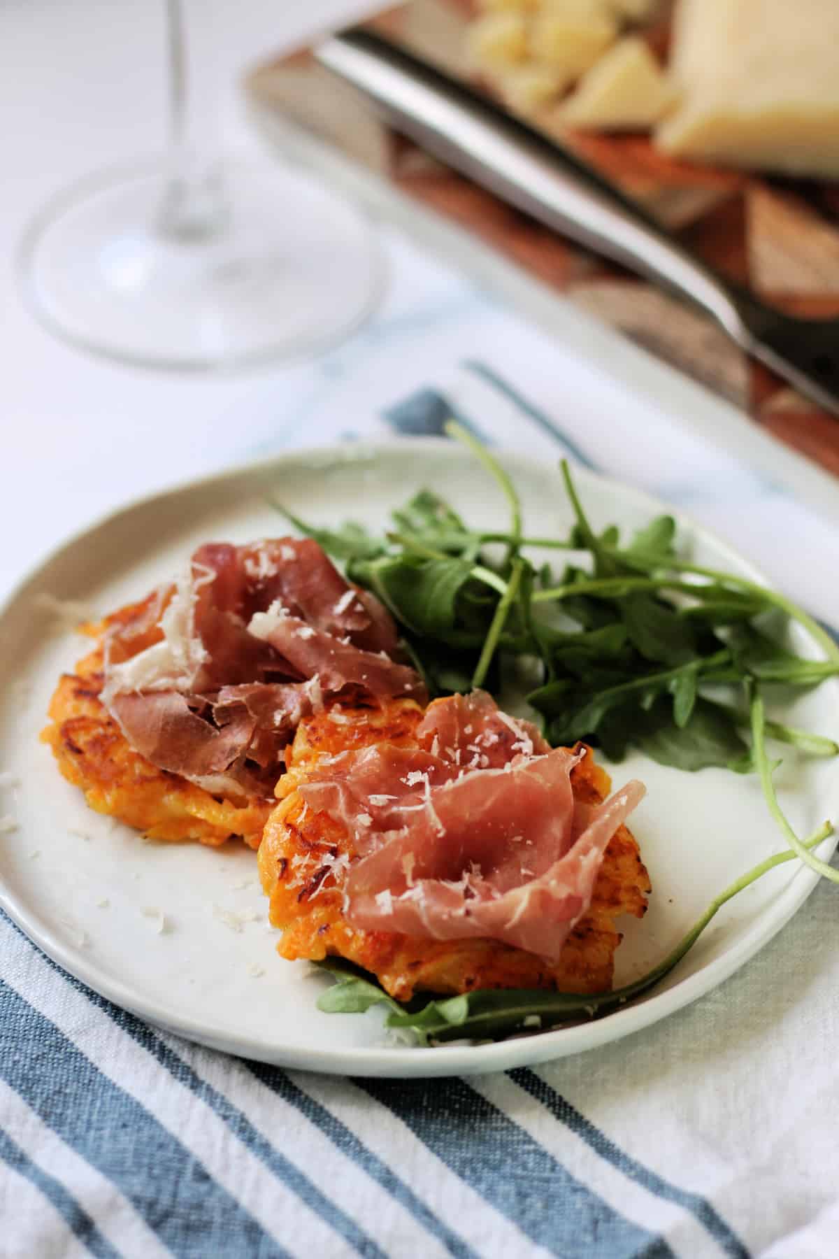 Close up of butternut squash fritters topped with proscuitto di San Daniele on an appetizer plate.