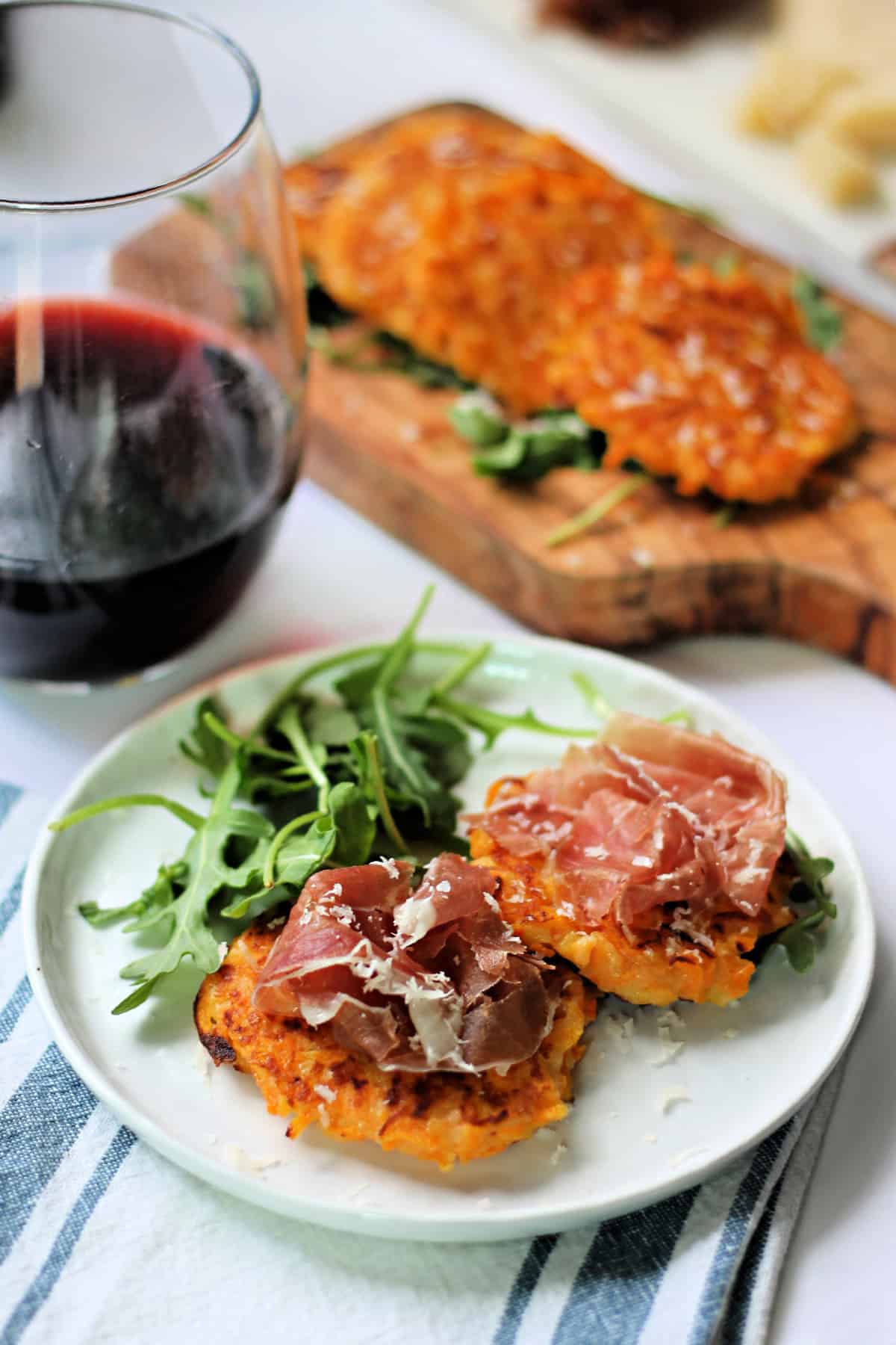 Butternut squash fritters topped with proscuitto on an appetizer plate.