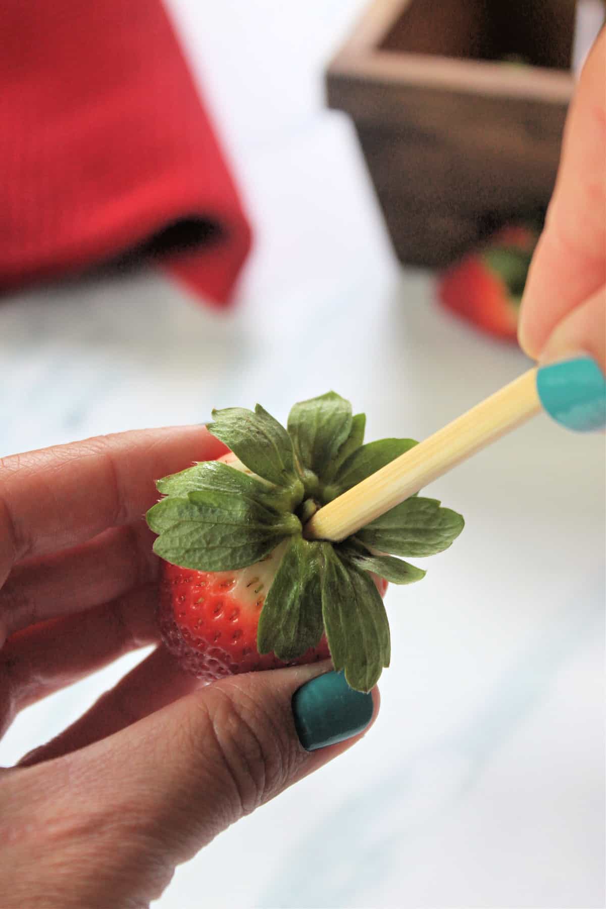 Process shot of inserting skewer into leafy end of strawberry for making strawberry roses.