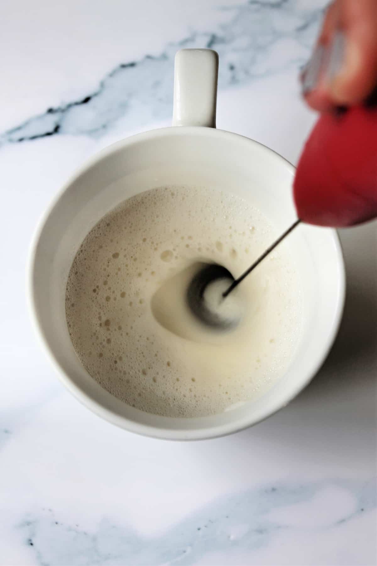 Milk being frothed in a white mug with frother.