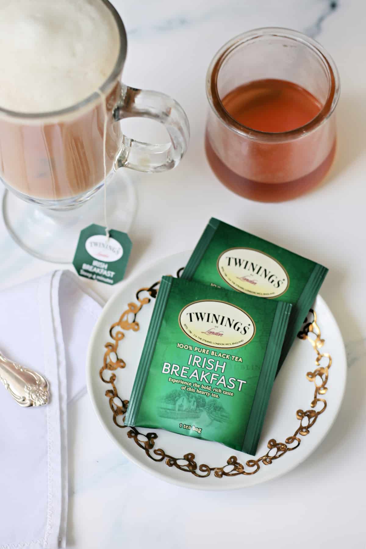 Irish Breakfast Tea bags on a small white plate next to tea latte.