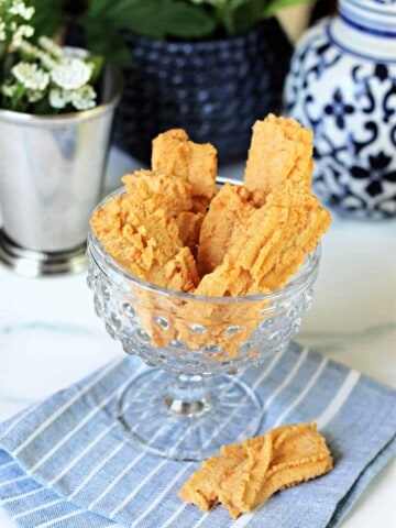 Southern Cheese Straws in a clear glass dish with decorative elements surrounding.