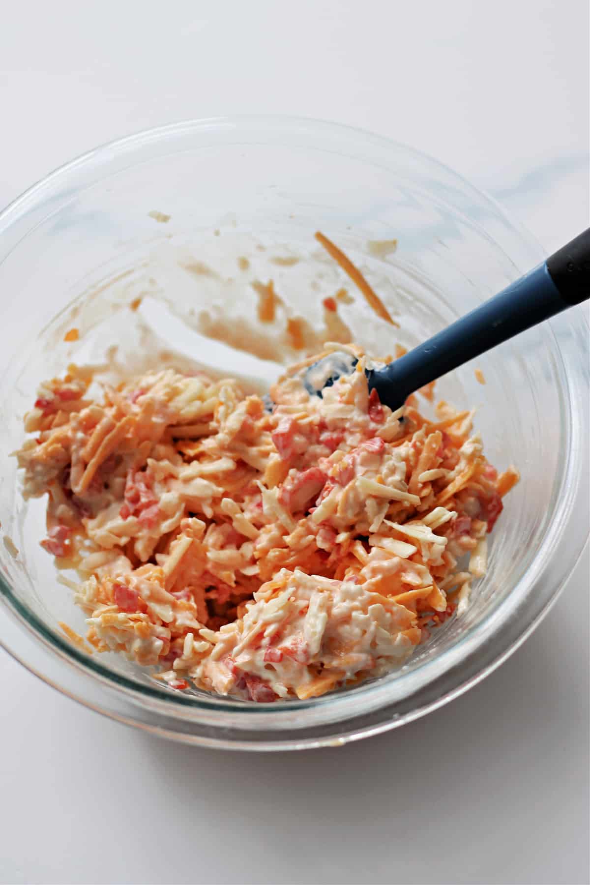 Ingredients for pimento cheese recipe being mixed in a glass bowl.