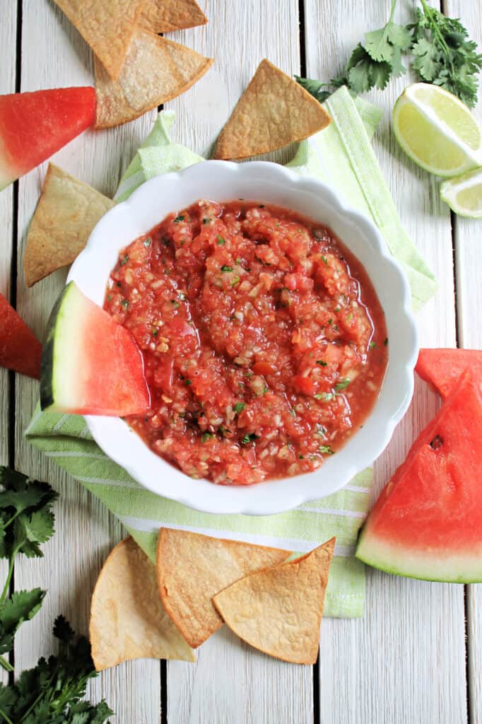 Grilled Watermelon Salsa in a white bowl surrounded by watermelon slices and tortilla chips.