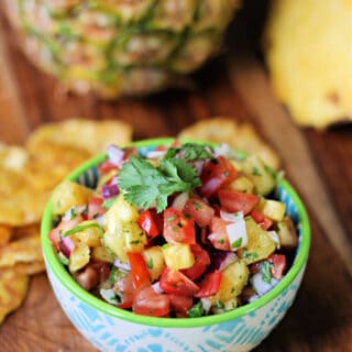 Pineapple Pico de Gallo salsa in a small bowl with plantain chips surrounding it and a pineapple in the background.