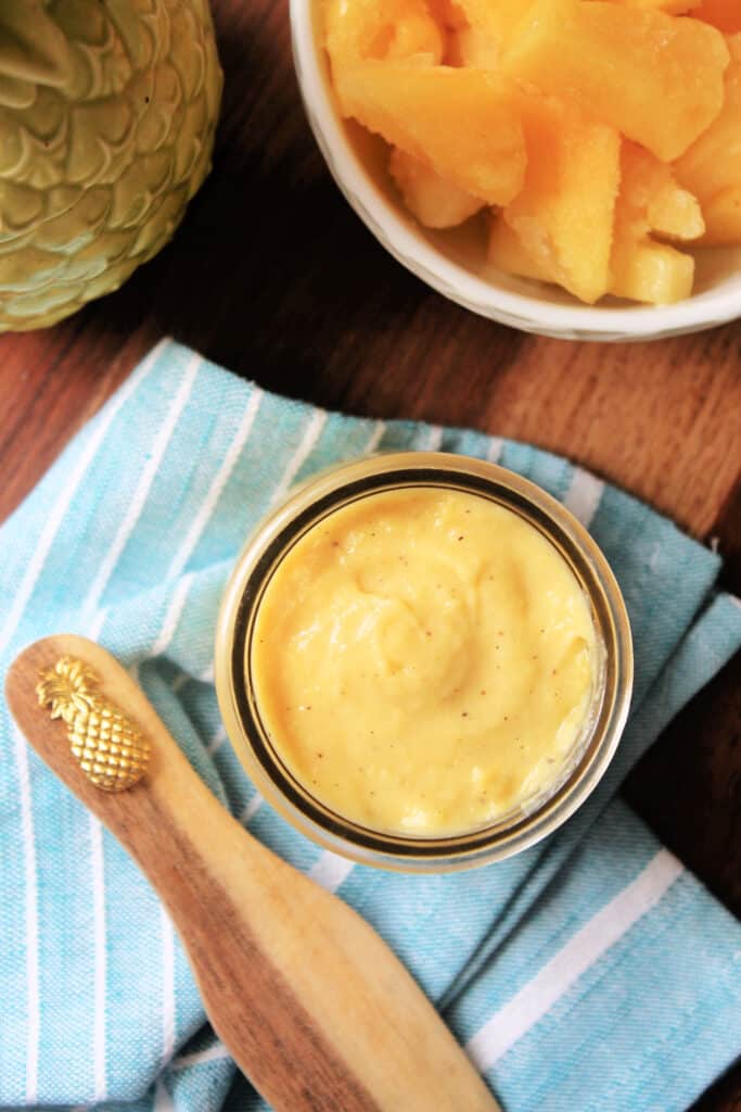 Overhead view of Pineapple Curd in a glass jar with a small wooden spreader next to it.