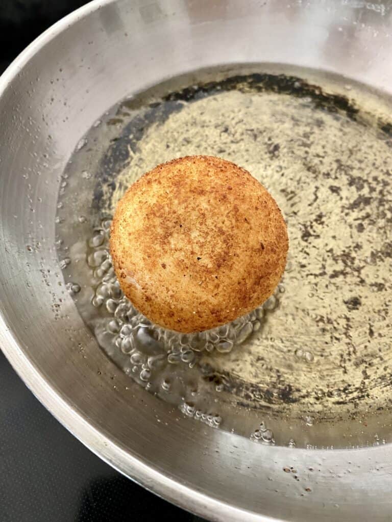Frying a Papa Rellena in oil in a skillet.