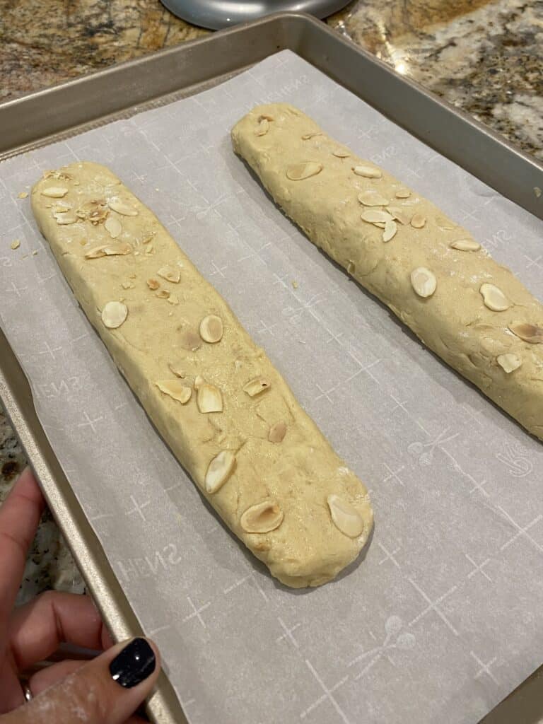 Two shaped Amaretto Biscotti dough logs on a parchment lined baking pan.