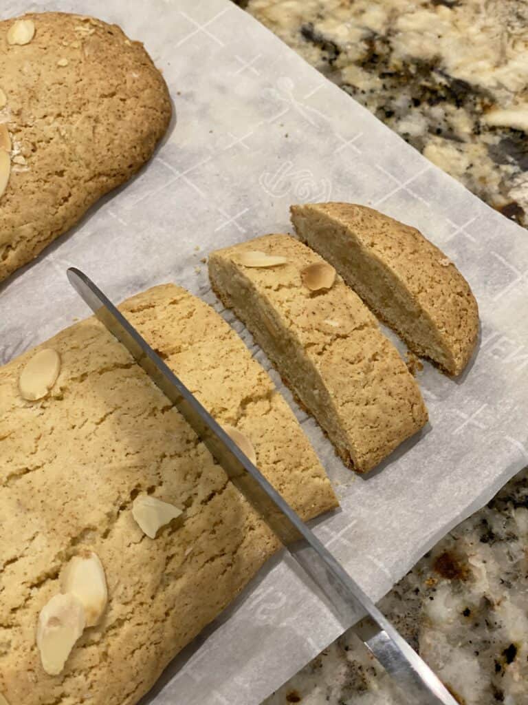 Using a serrated knife to slice baked Amaretto Biscotti logs.