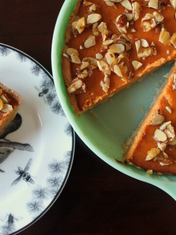 A slice of Amaretto Pumpkin Pie on a black and white plate next to the rest of the pie in a jadeite pie dish.
