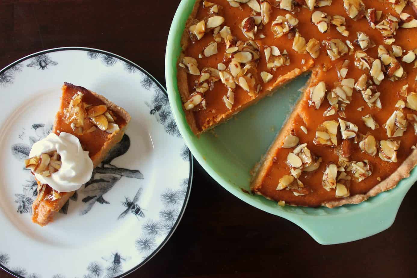 A slice of Amaretto Pumpkin Pie on a black and white plate next to the rest of the pie in a jadeite pie dish.