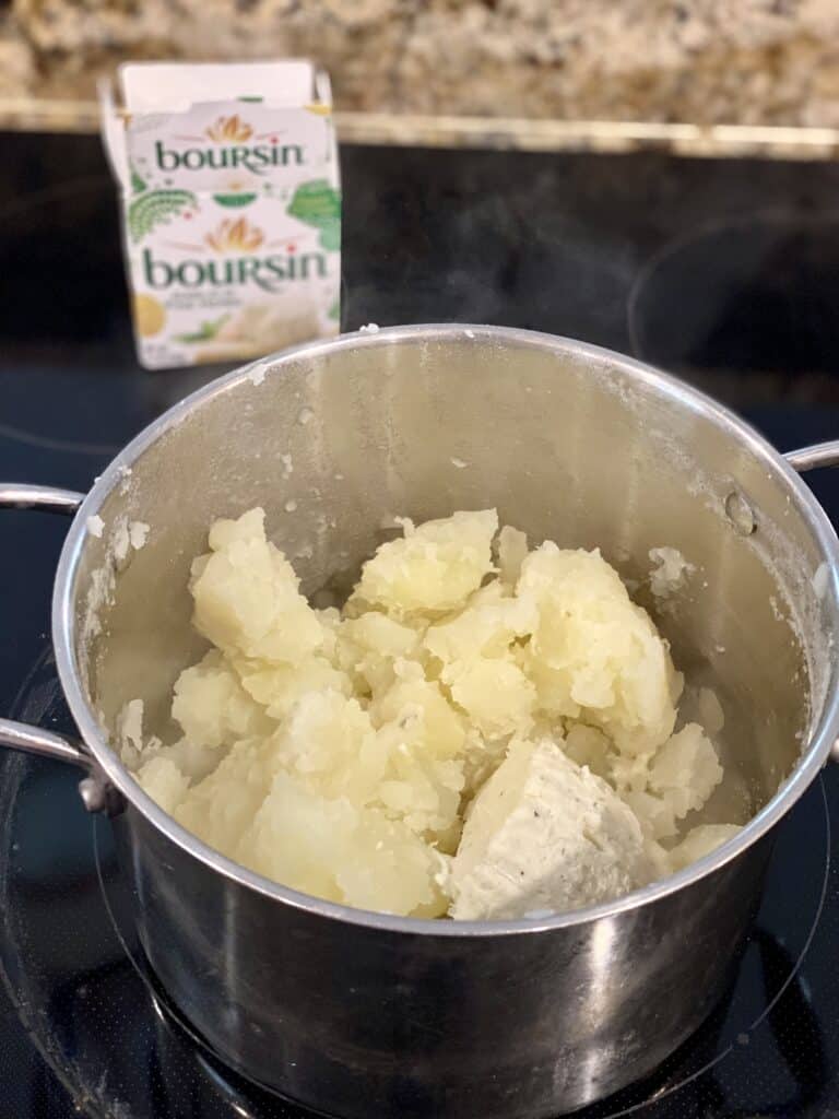 Cooked potatoes and Boursin cheese in a pot on the stove.