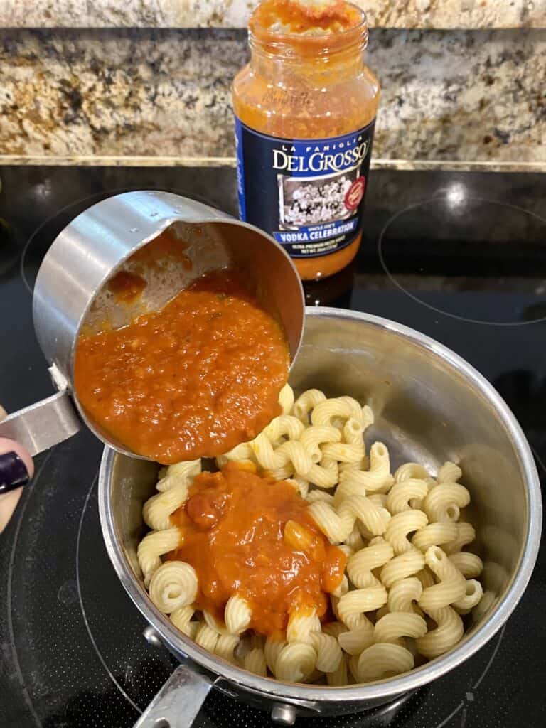 Pouring sauce into pot with cooked pasta.