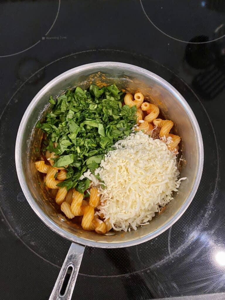 Spinach and cheese added to pasta with sauce in a pot.