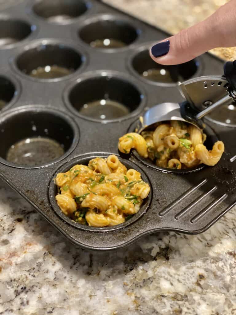 Using an ice cream scoop to put pasta in muffin tin.