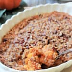 A silver spoon scooping a serving of Ruth's Chris Sweet Potato Casserole from a white casserole dish.