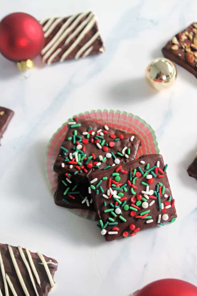 A stack of Christmas sprinkle-covered Chocolate Covered Graham Crackers on a marble surface.