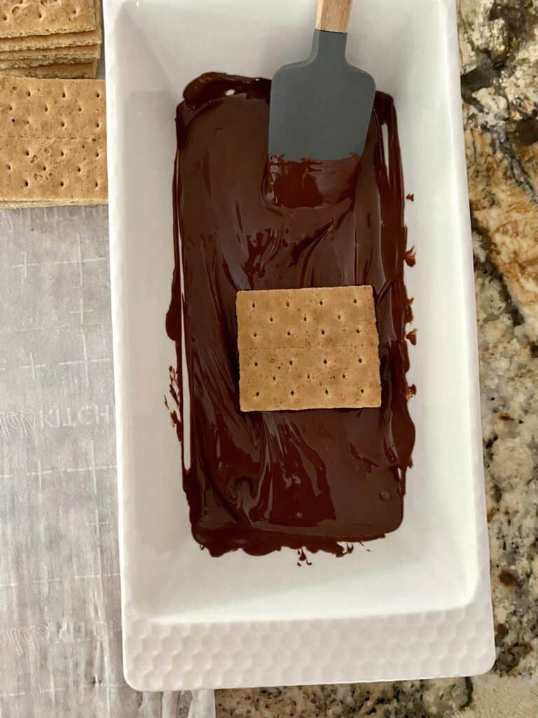A graham cracker placed in a dish of melted chocolate.