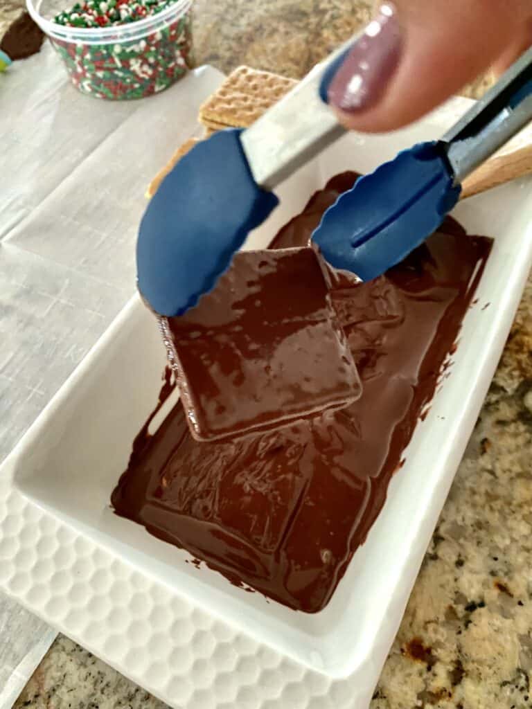 Lifting a chocolate covered graham cracker out of my melted chocolate with tongs.