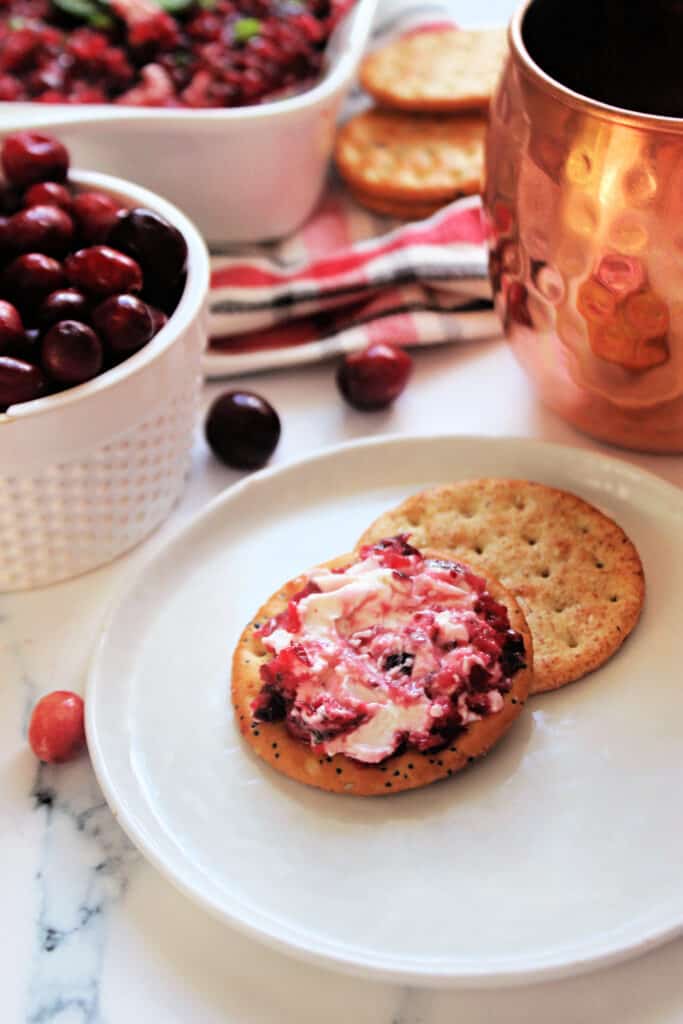 Cranberry Jalapeno Dip spread onto a cracker on a white appetizer plate.