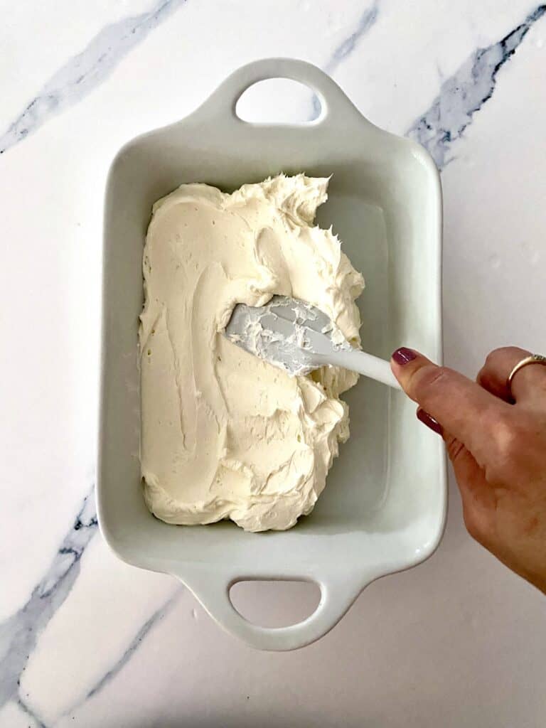 Smoothing cream cheese mixture for Cranberry Jalapeno Dip into a white serving dish.