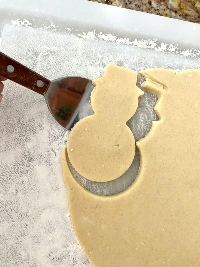 Using a cooke spatula to remove cut out snowman sugar cookie shape from dough.