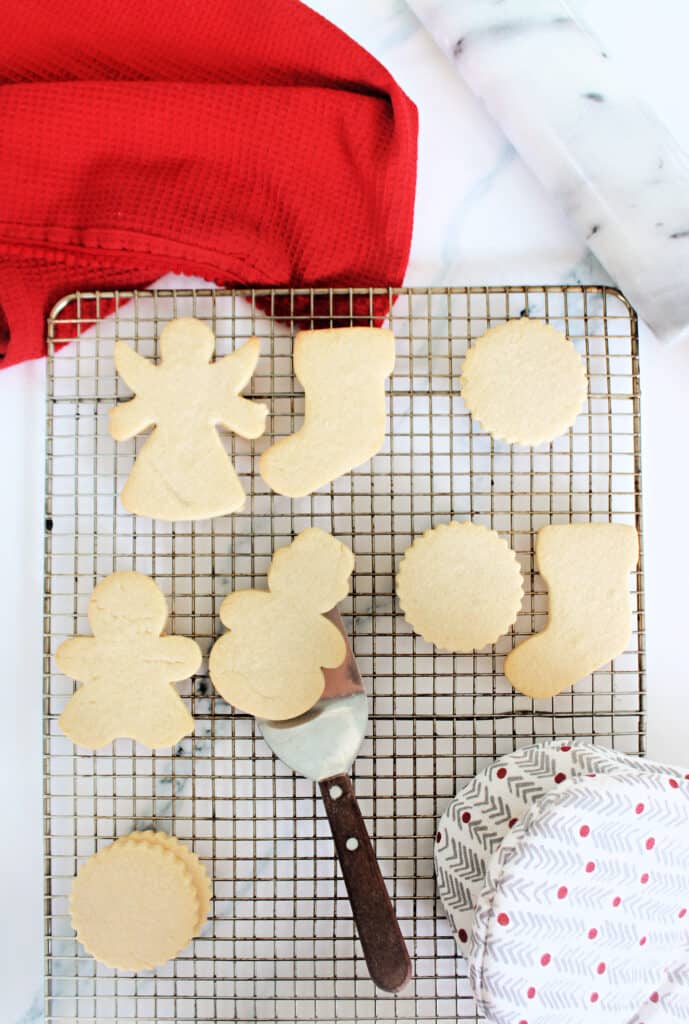 A variety of No Spread Sugar Cookies on a cooling rack, with one being lifted by a cookie spatula.