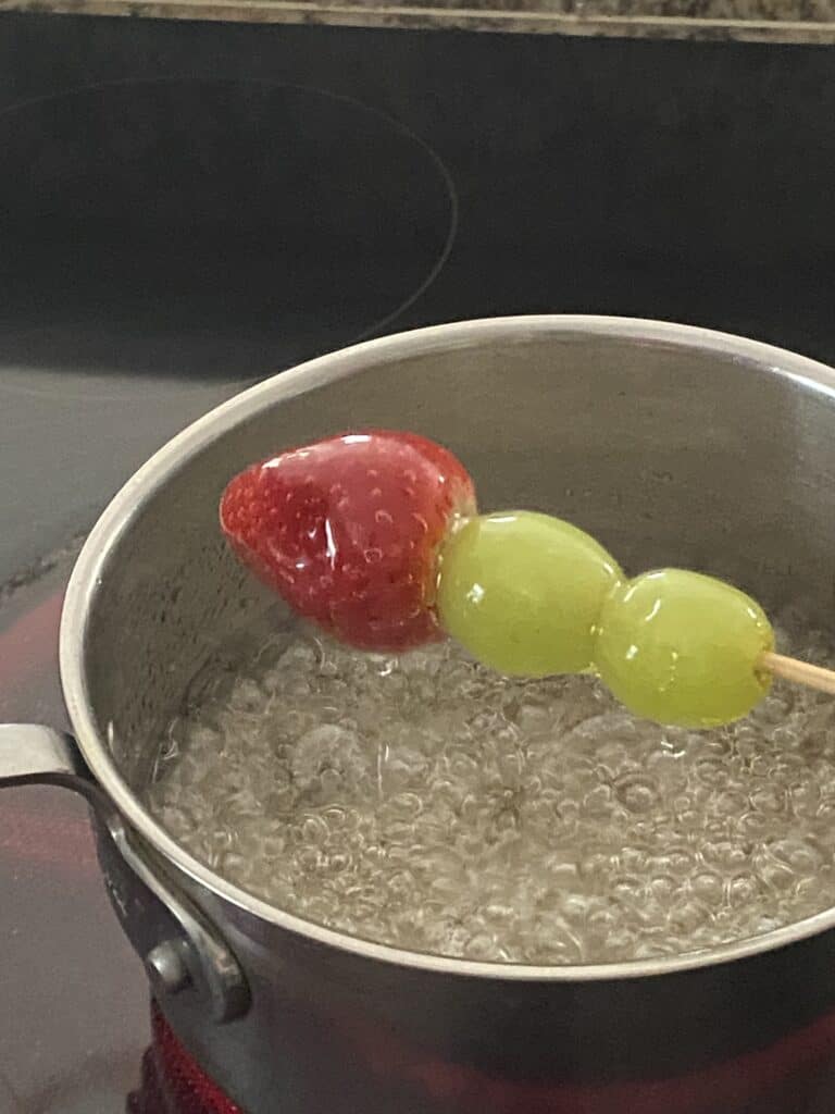 Dipping fruit skewers into sugar syrup for Tanghulu fruit.