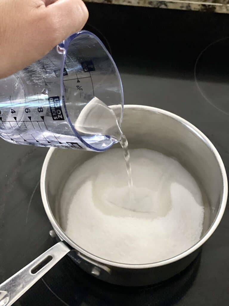 Adding ½ cup water to granulated sugar in a saucepan for tanghulu recipe.