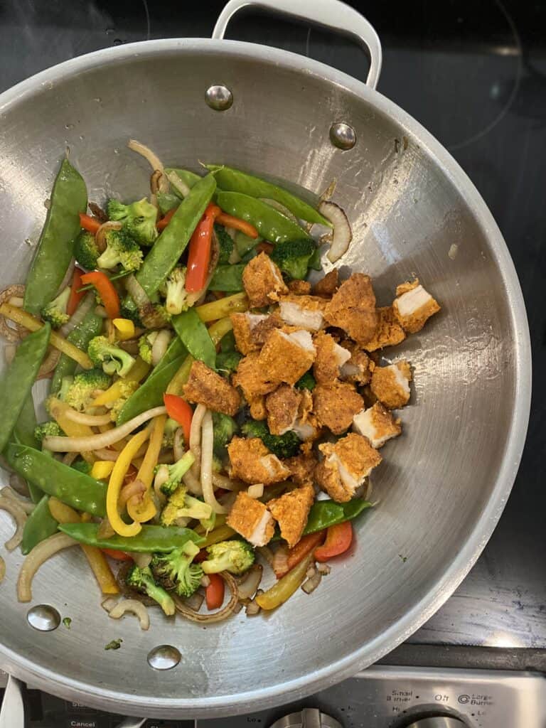 Chopped chicken tenders added to wok for stir fry.
