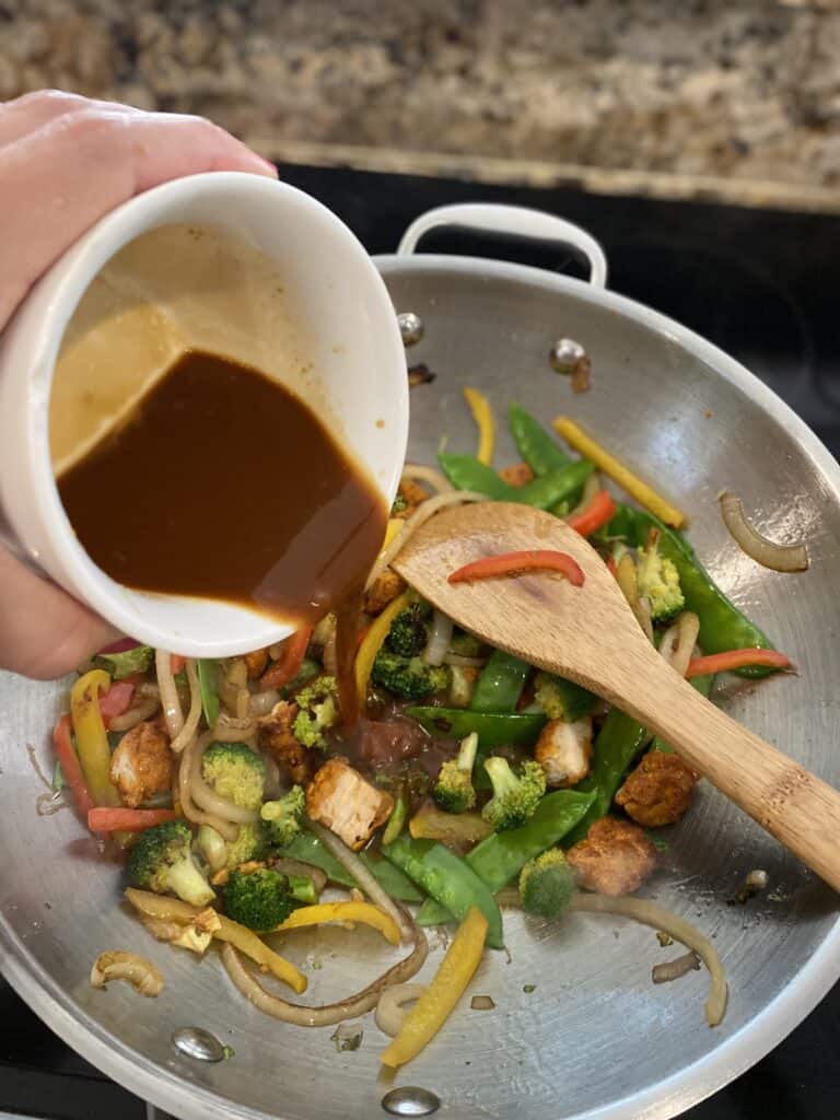 Pouring sauce mixture over vegetables in wok for stir fry.