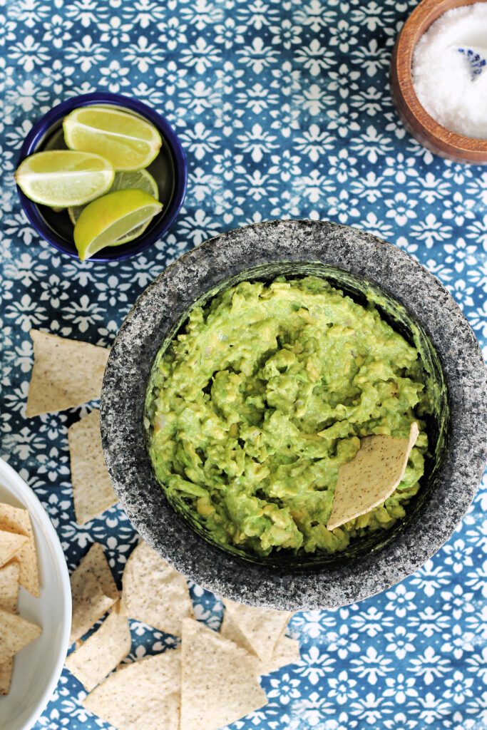 Overhead shot of 4-ingredient guacamole in a molcajete with scattered tortilla chips beside it.