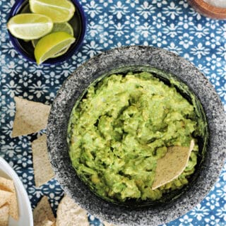 Overhead shot of 4-ingredient guacamole in a molcajete with scattered tortilla chips beside it.