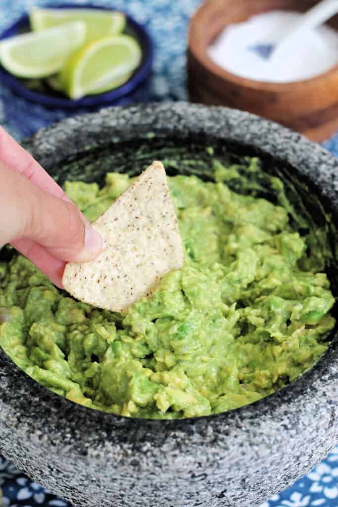 Hand dipping a tortilla chip into a molcajete of guacamole to show texture.