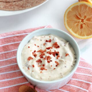 Bacon aioli in a small white ceramic ramekin atop an orange and white striped napkin.