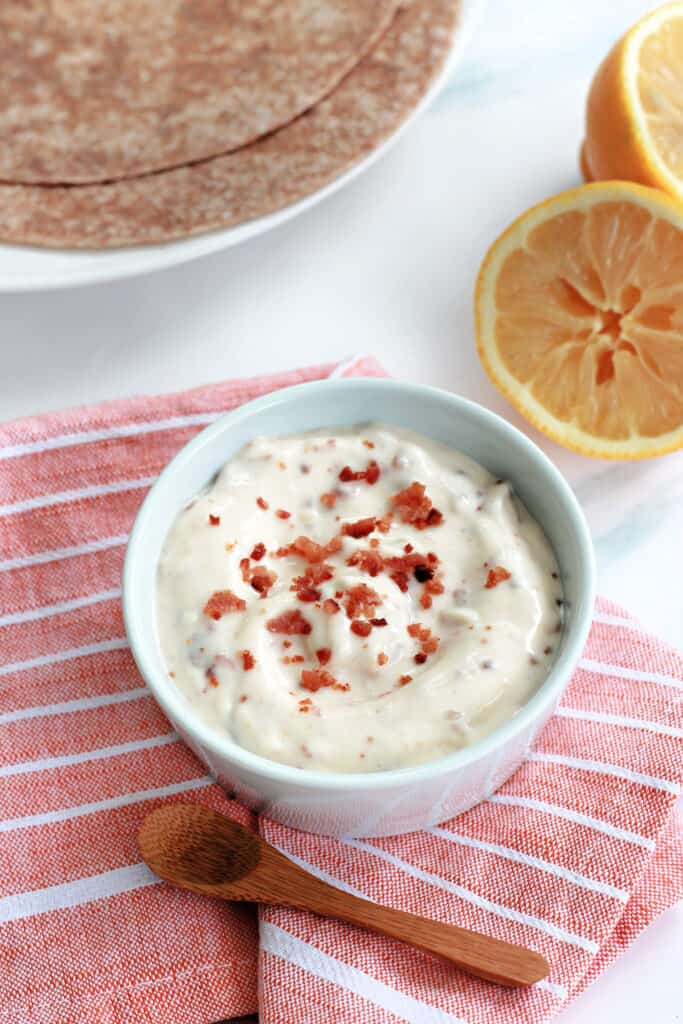 Bacon aioli in a small white ceramic ramekin atop an orange and white striped napkin.