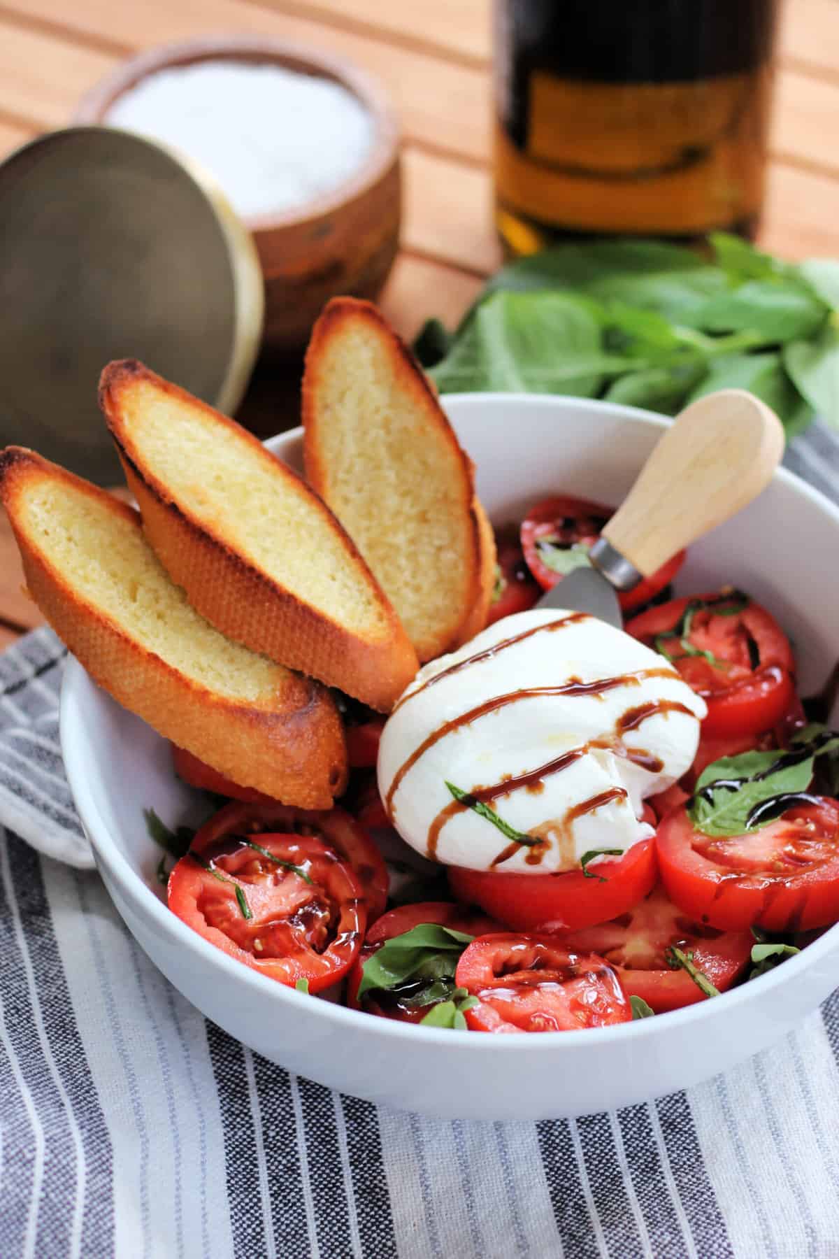 Burrata Caprese in a white bowl with toasted bread slices.