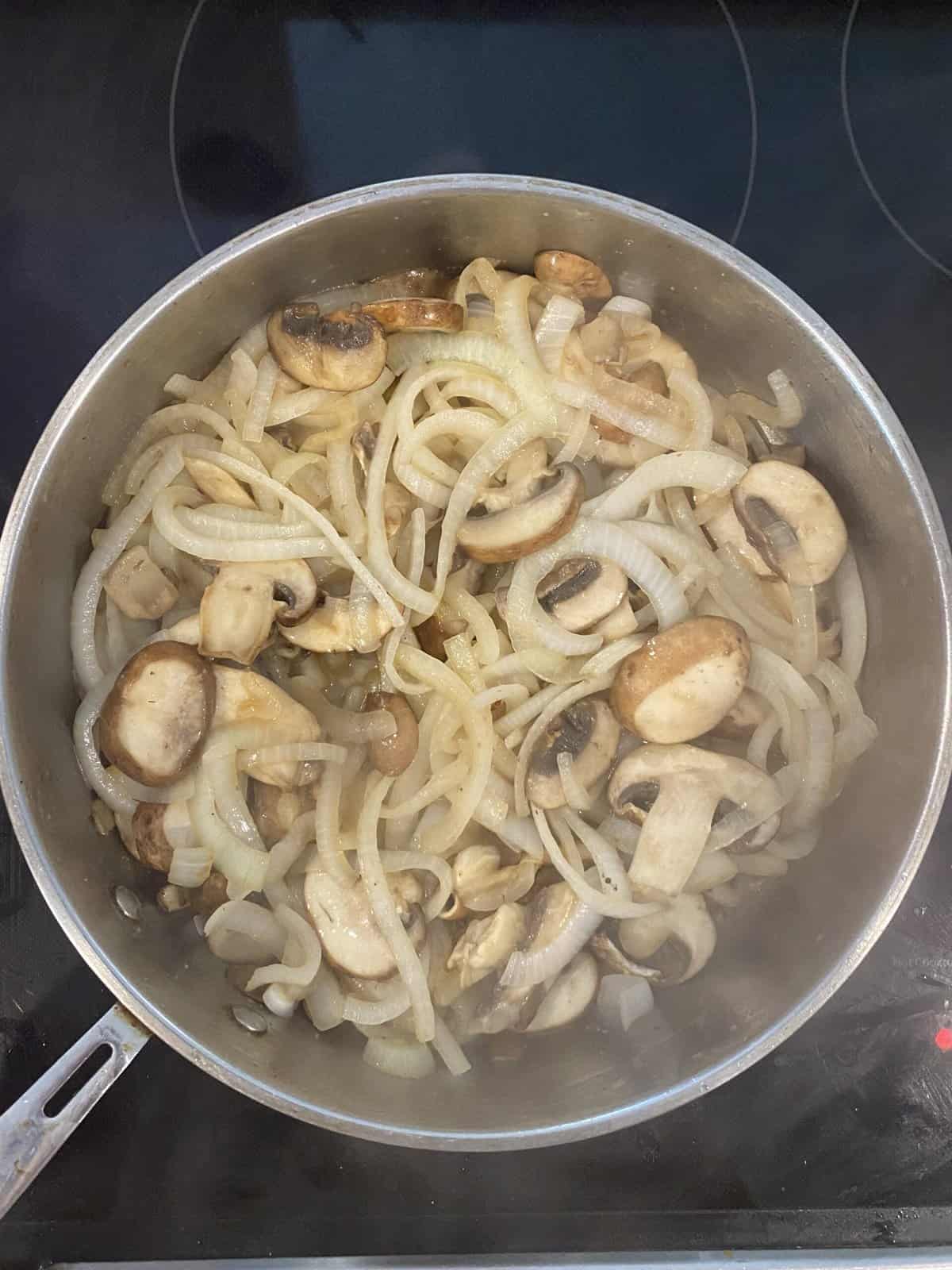 A large pan filled with onions and mushrooms about 5 minutes into the caramelization process.