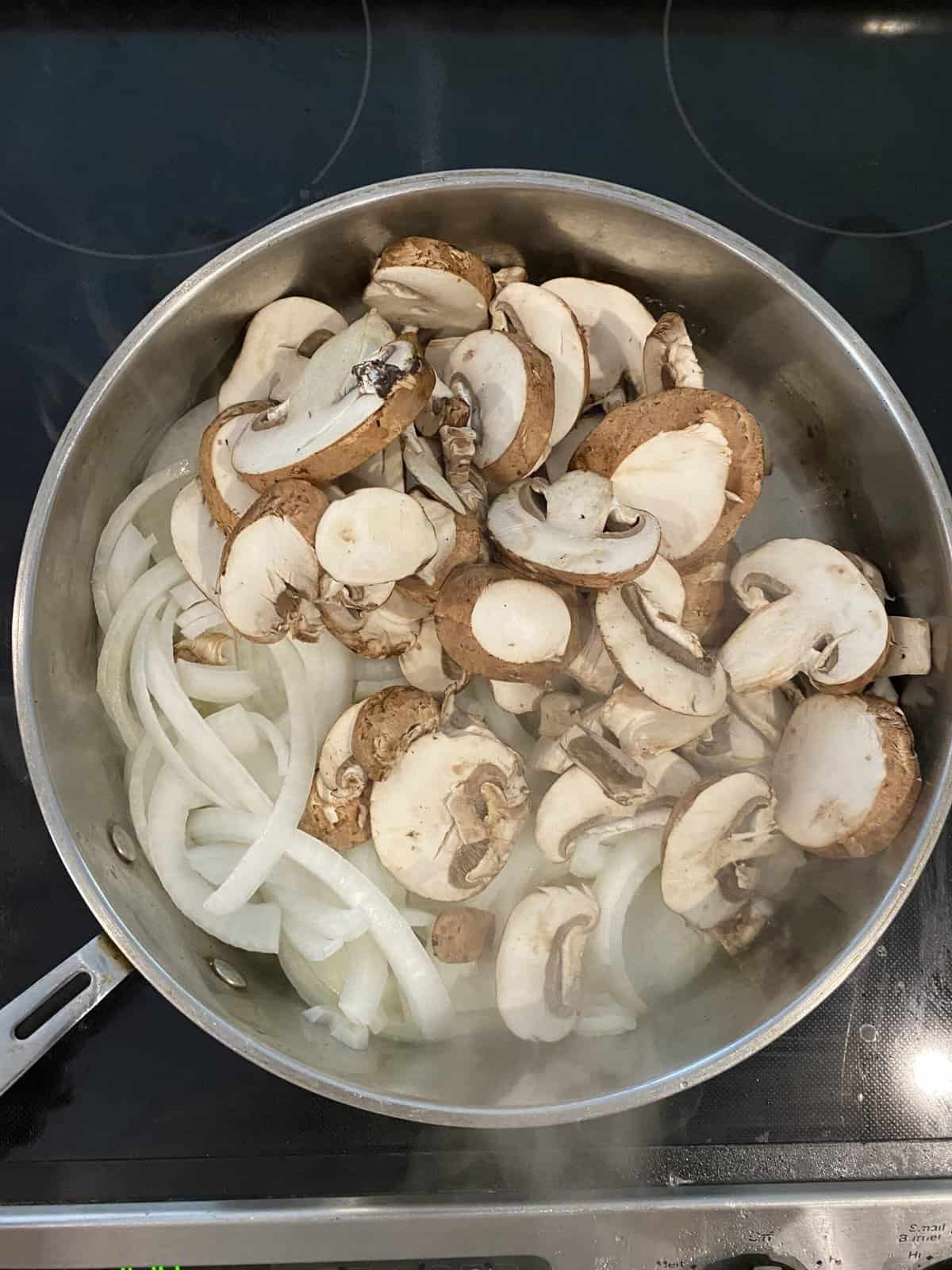 A large pan filled with onions and mushrooms at the beginning of the caramelization process.