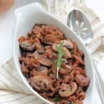 Caramelized onions and mushrooms in a white dish with a silver serving spoon beside it.