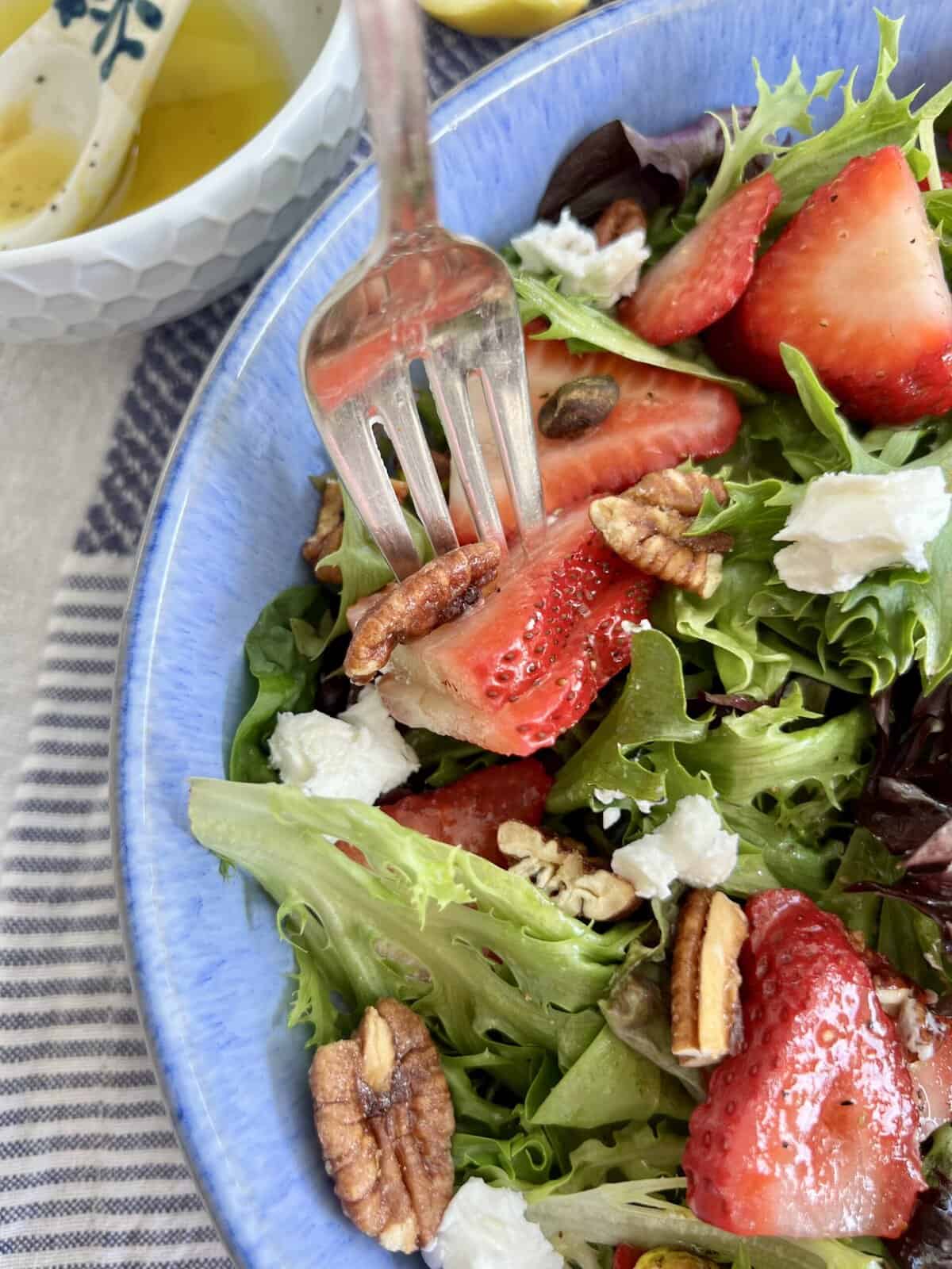 Close up of fork with strawberry, pecan and salad.