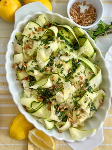 Zucchini Ribbon Salad in a white serving dish surrounded by lemons and other ingredients.