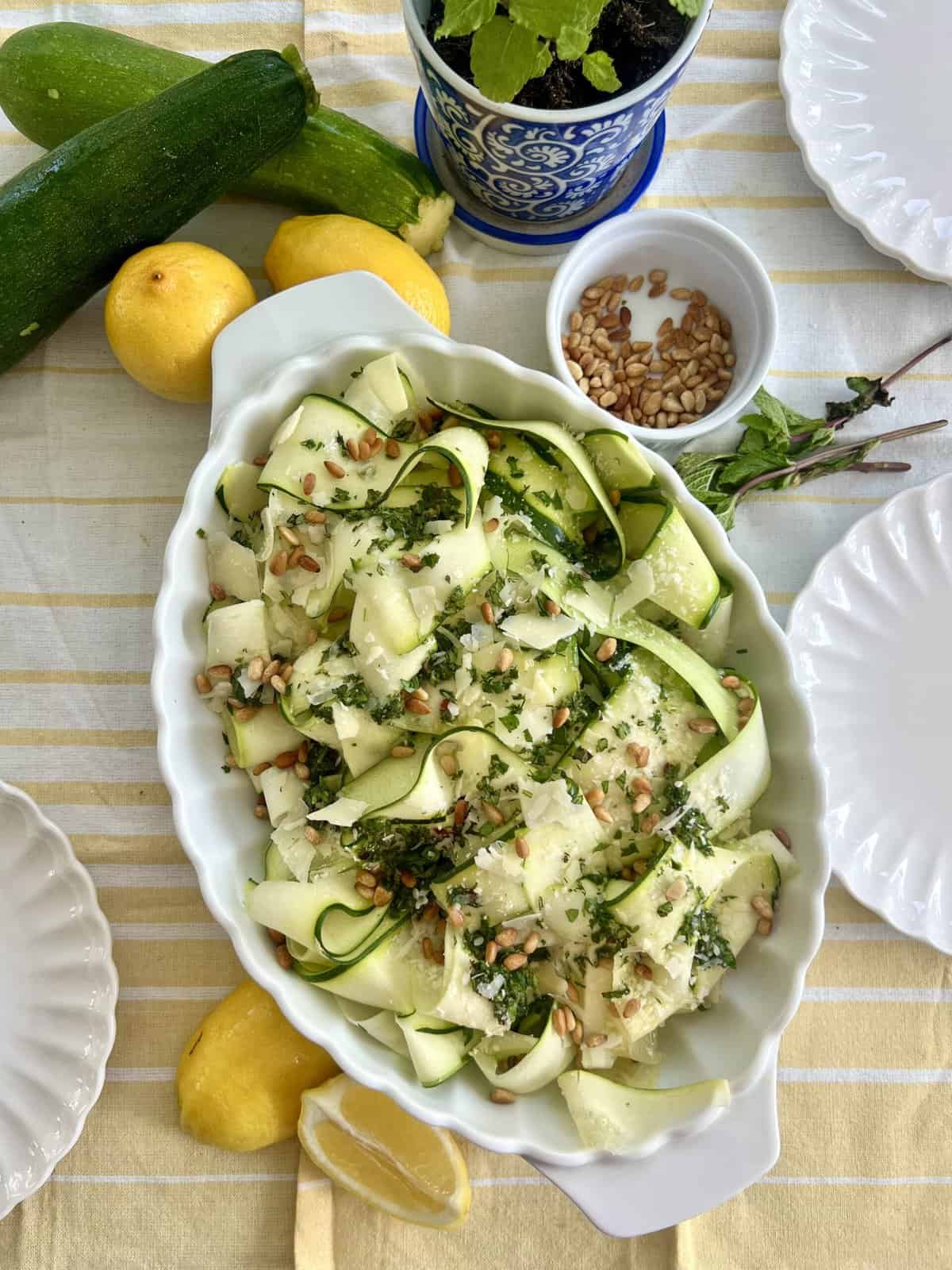 Zucchini Ribbon Salad in a white serving dish surrounded by lemons and other ingredients.