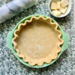 An overhead image of raw pie dough in a green pie dish.