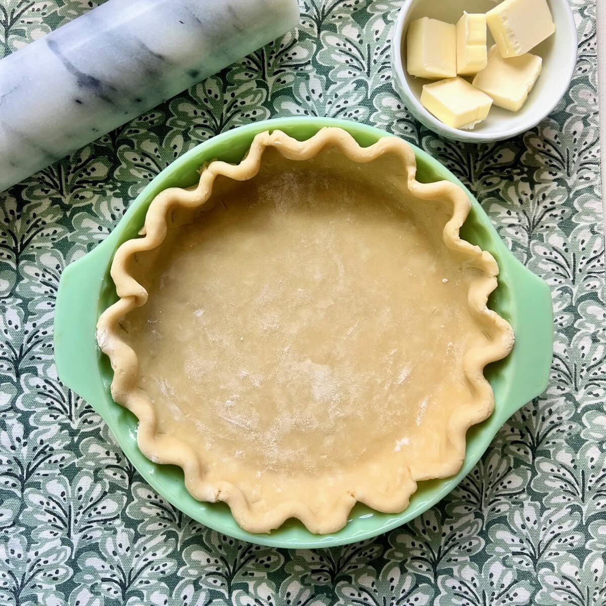 An overhead image of raw pie dough in a green pie dish.