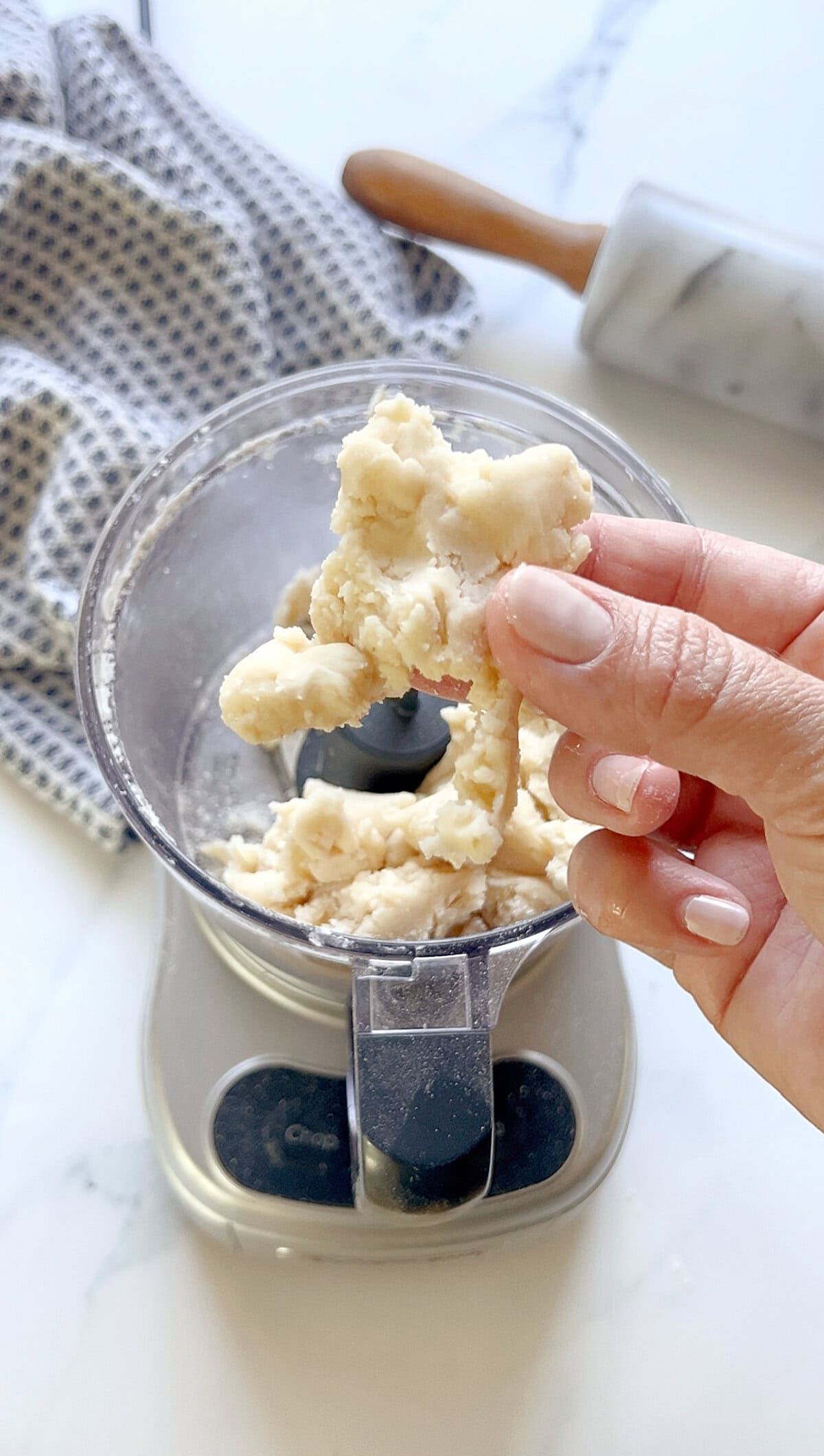 Holding up a piece of pie dough that has been made in the food processor to show texture.