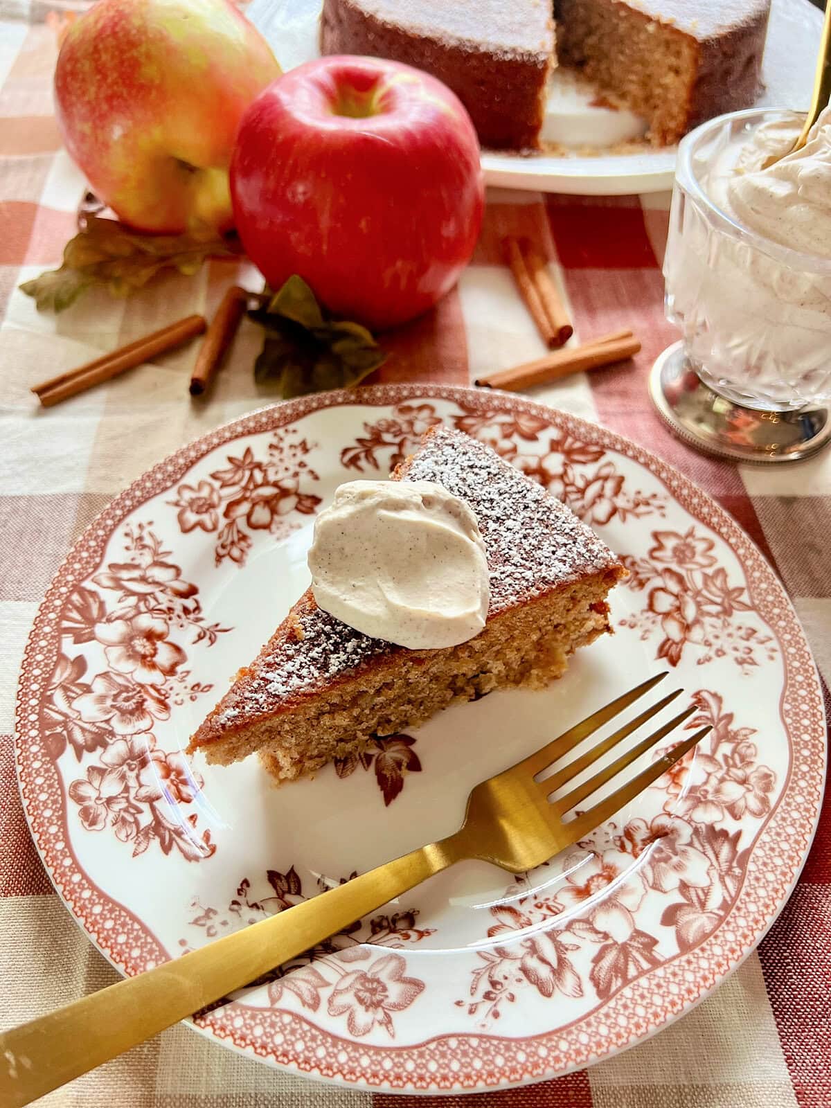 A slice of apple spice cake with a dollop of cinnamon whipped cream on a seasonal plate.